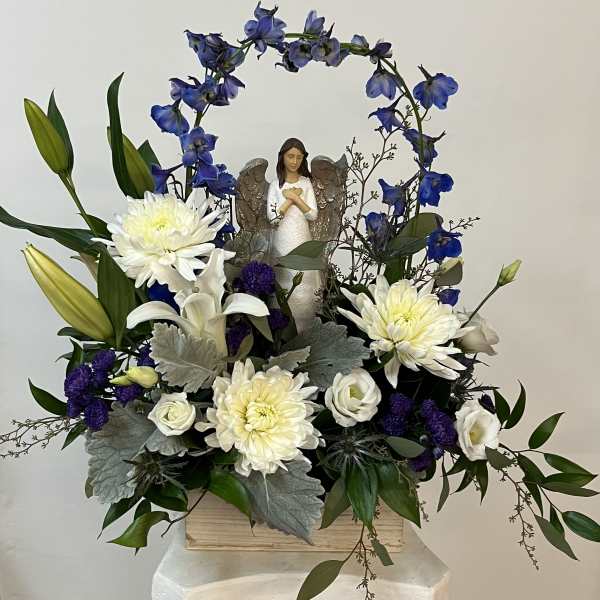 White and blue floral arrangement with an angel figurine in a wooden box