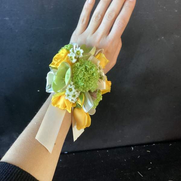 Yellow and green wrist corsage with ribbon ties on a hand