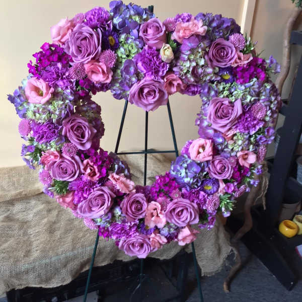 Heart-shaped floral wreath with purple and pink roses on a stand