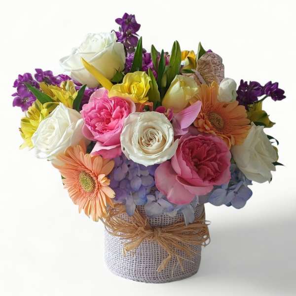 Colorful mixed flower arrangement with roses, gerbera daisies, and hydrangeas in a burlap-wrapped vase
