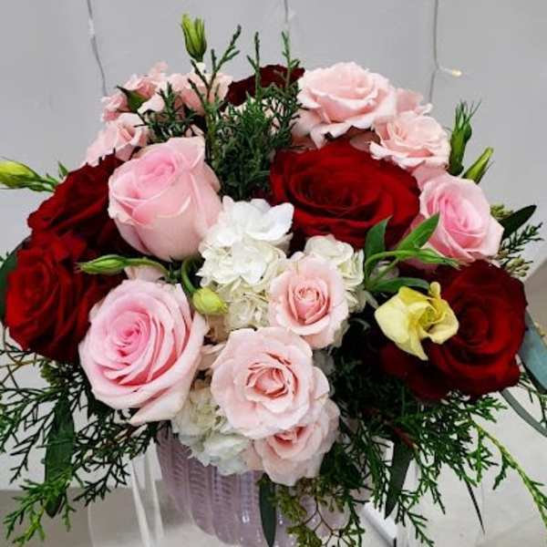 Round arrangement of red and pale pink roses with white blooms in a pink glass vase