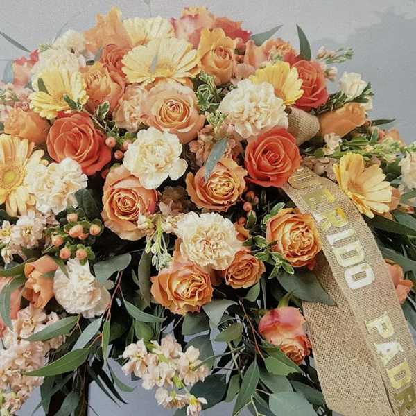 Orange and cream roses, carnations, and gerberas in a large spray with a burlap sympathy ribbon