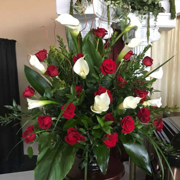 Large arrangement of red roses and white calla lilies in a dark pedestal vase