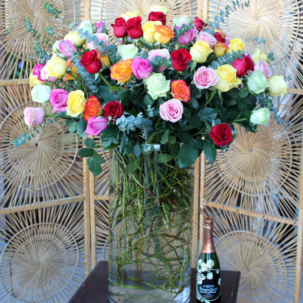 Mixed roses in a tall glass vase with a champagne bottle and candle