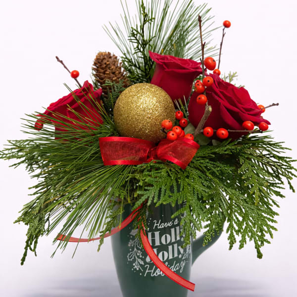 Holiday mug arrangement with red roses, pine branches, berries, and a gold ornament ball