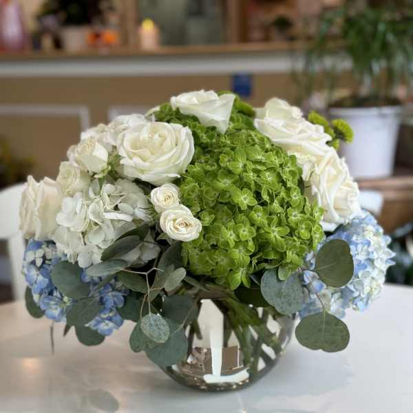 White roses and green hydrangeas in a glass vase with blue hydrangea accents