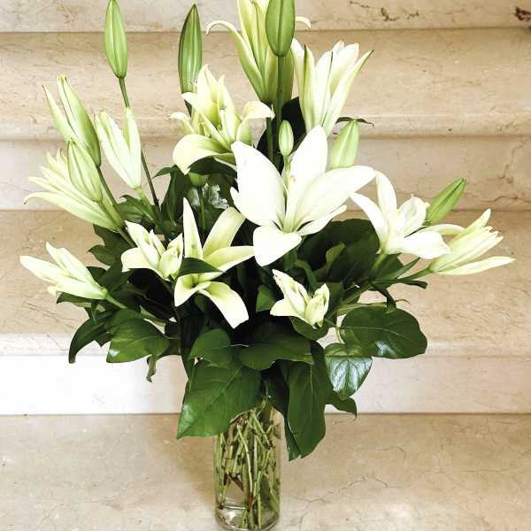 Tall white lilies beautifully arranged in a glass vase.