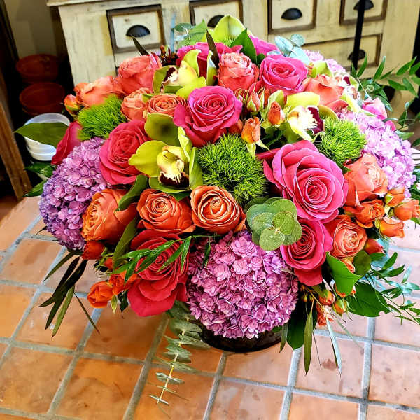 Mixed bouquet of pink and orange roses with purple hydrangeas in a low container