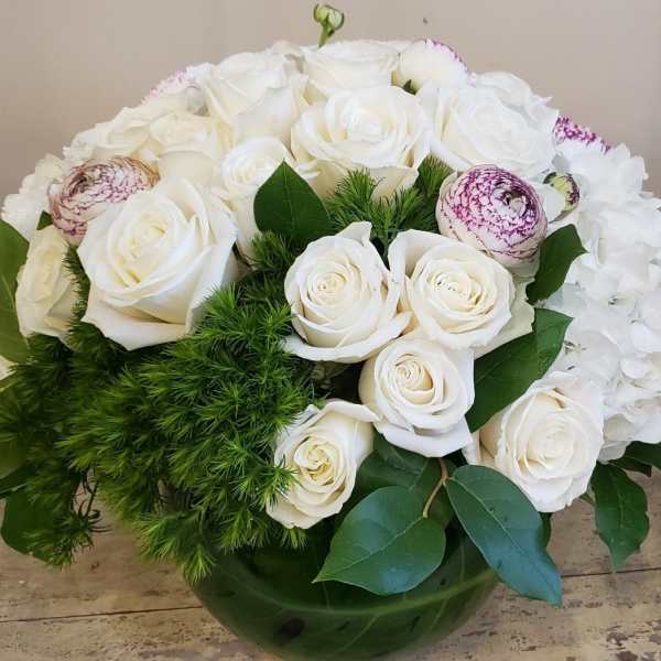White roses and hydrangeas in a green glass vase with greenery