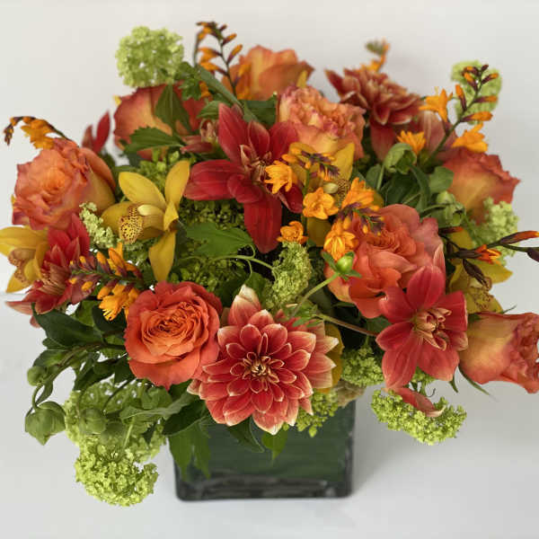 Orange and red mixed flowers arranged in a square glass vase