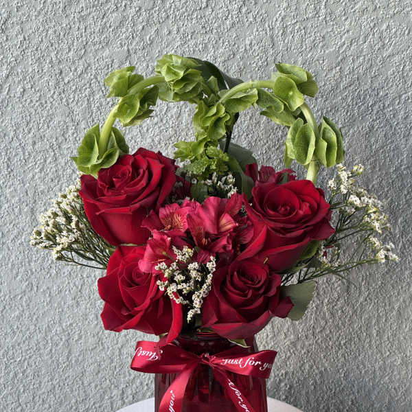 Red roses and pink flowers in a red vase with a ribbon