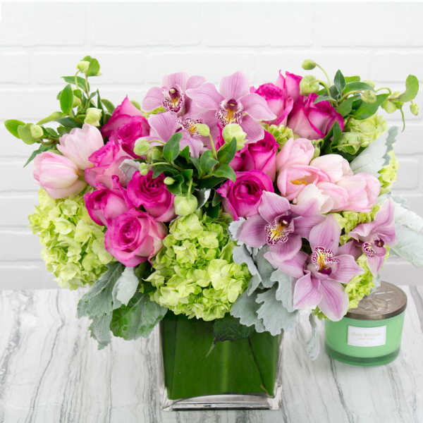 Compact pink and green flower arrangement with orchids, roses, and hydrangeas in a square glass vase