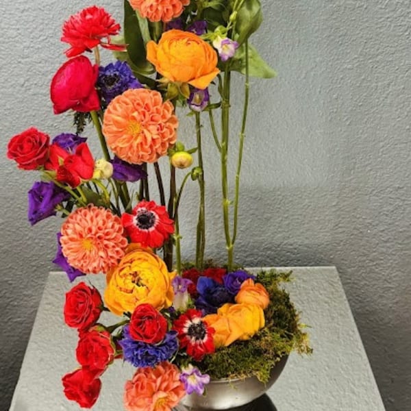 Tall colorful floral arrangement with roses, dahlias, and purple blooms in a metal vase