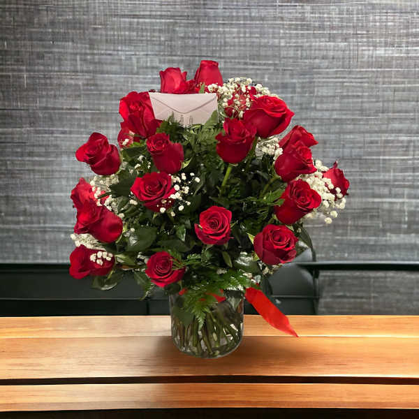 Red roses arranged in a clear glass vase with baby's breath and a red ribbon