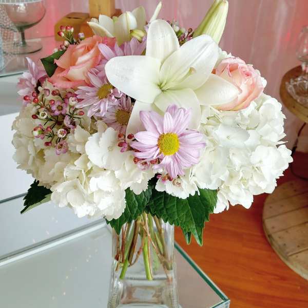Bouquet of white hydrangeas, pink roses, and lilies in a clear glass vase