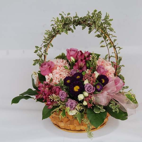 Basket arrangement of pink and purple flowers with a ribbon and arch handle