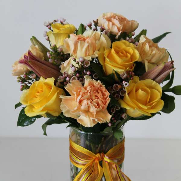 Yellow roses and peach carnations in a clear glass vase with a yellow ribbon bow