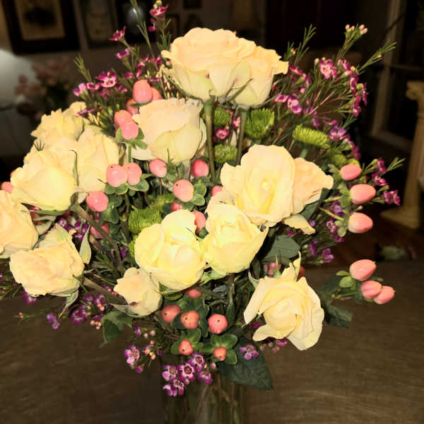 Yellow roses in a clear glass vase with pink filler flowers