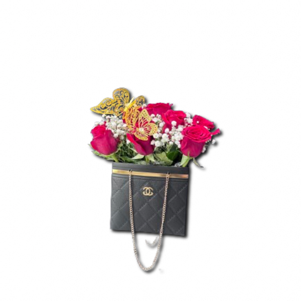 Red roses and white filler flowers arranged in a black quilted handbag with gold butterfly accents.