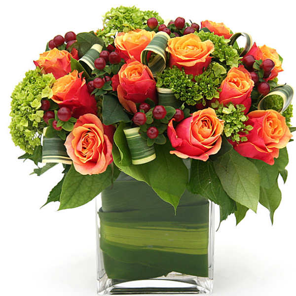 Orange roses arranged in a clear square vase with green accents