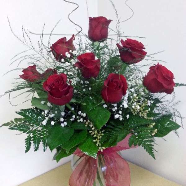 Red roses arranged in a clear glass vase with a pink ribbon