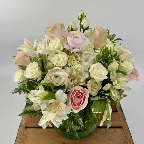 Compact arrangement of white and pale pink roses, hydrangeas, and lilies in a round glass vase