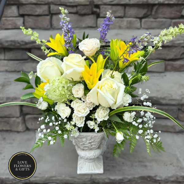 Tall white and yellow flower arrangement with roses and lilies in a white pedestal urn