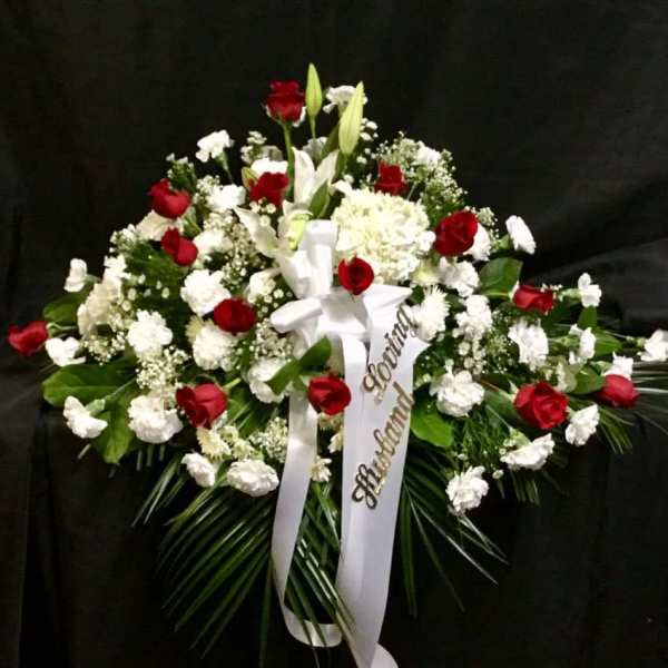 Red and white funeral spray with ribbon on a dark background