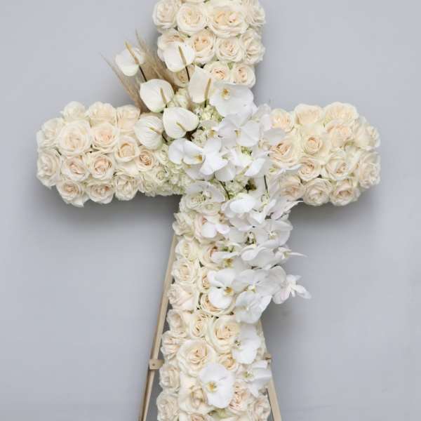 Cross-shaped floral arrangement of cream roses and white orchids on an easel
