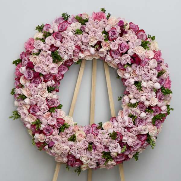 Circular floral wreath of pink and lavender roses on a wooden stand