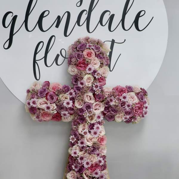 Cross-shaped floral arrangement in pink and purple roses with small daisy-like blooms