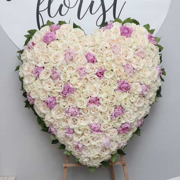 Heart-shaped floral arrangement of white and pink roses on an easel