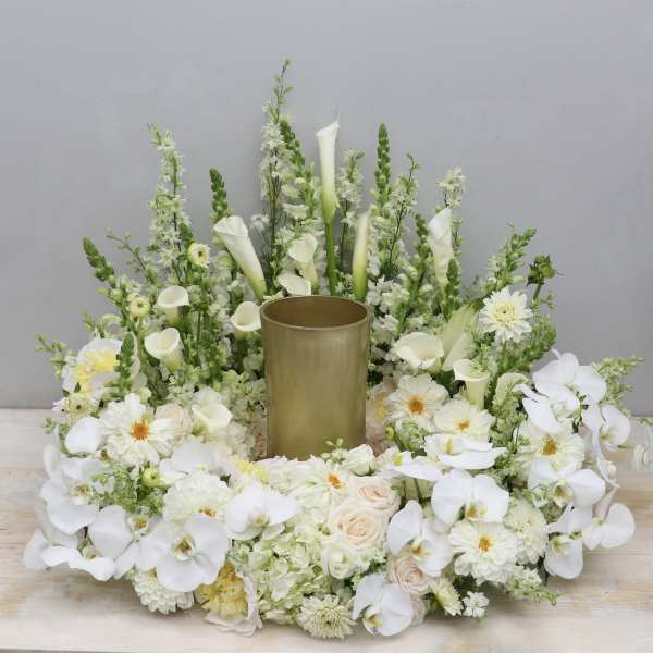 White floral arrangement with orchids, calla lilies, and roses around a gold vase