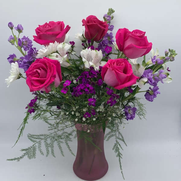 Vase arrangement with hot pink roses, purple flowers, and white blooms in a frosted pink glass vase