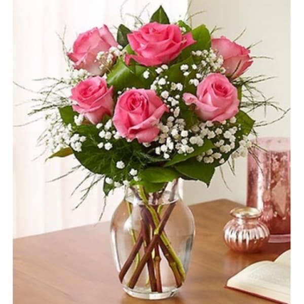 Pink rose bouquet with white filler flowers arranged in a clear glass vase on a wooden table