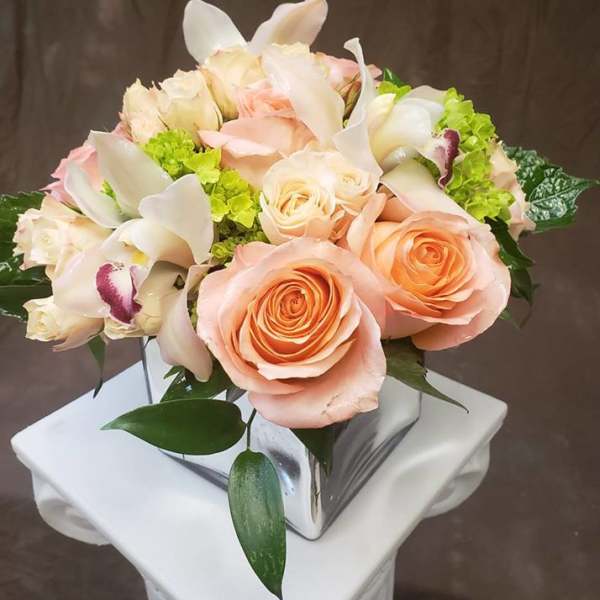 Peach roses and white orchids in a square glass vase