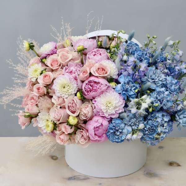 Large hatbox arrangement of pink roses and peonies with blue and white blooms in a split-color design