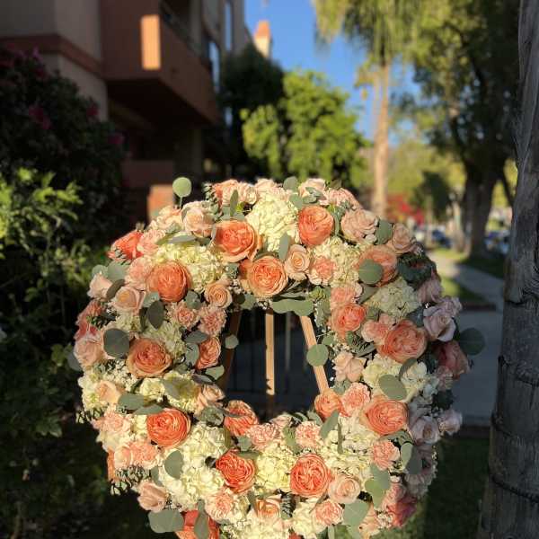 Large peach and white rose wreath on a wooden easel outdoors in sunlight