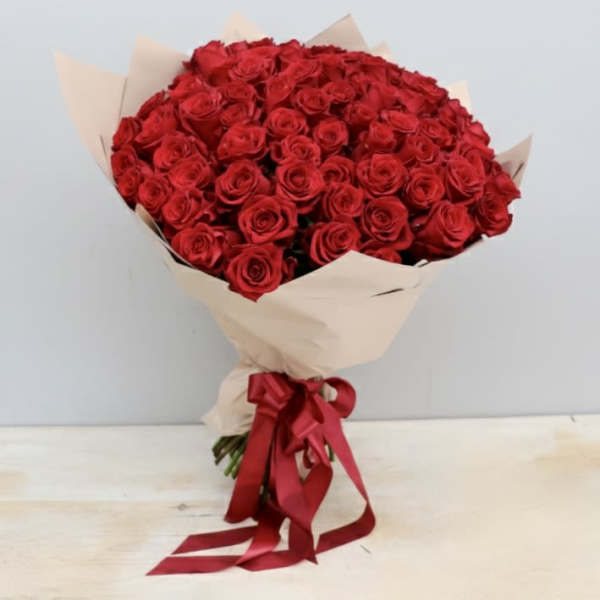 Large bouquet of red roses wrapped in beige paper with a red ribbon bow