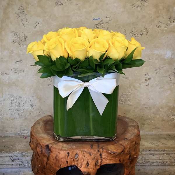 Yellow roses arranged in a square glass vase with a white ribbon