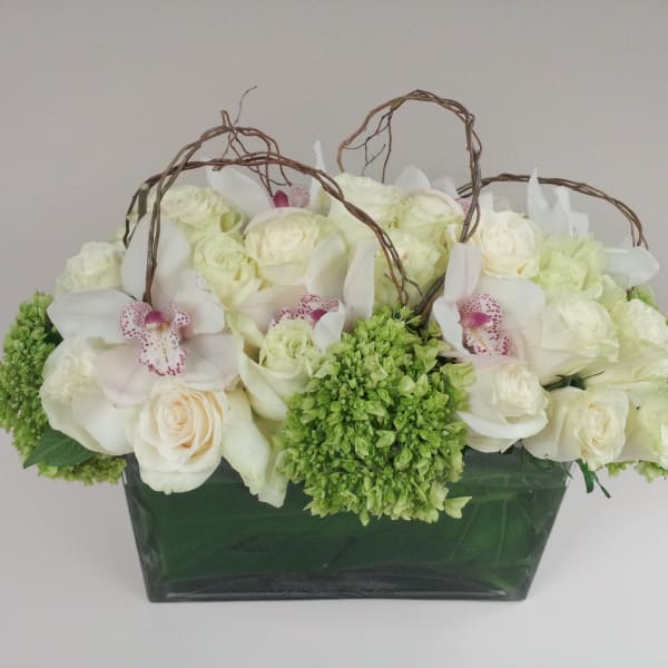 White roses and orchids arranged in a green vase with twig handles