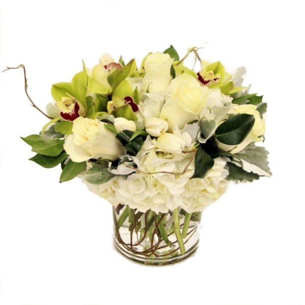 Low arrangement of white roses, hydrangeas, and green orchids in a clear glass vase