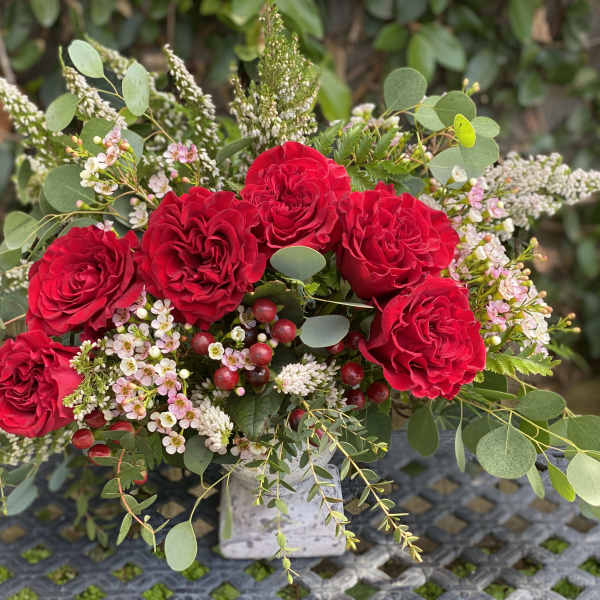 Red roses arranged with pink filler flowers in a square vase