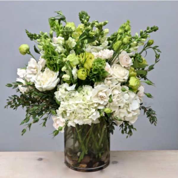 Tall arrangement of white hydrangeas and roses with bright green accents in a clear glass cylinder vase