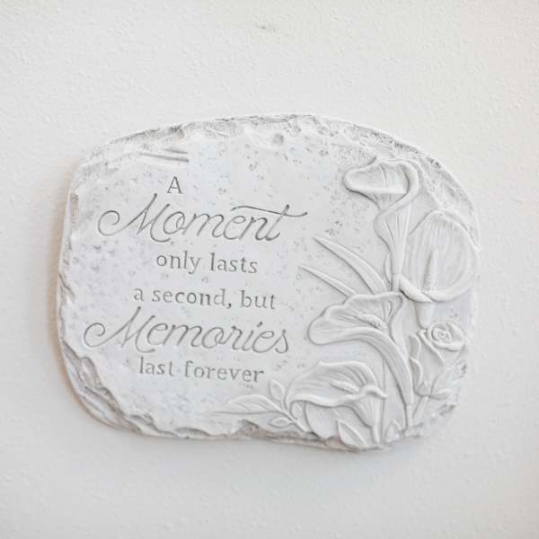 White stone plaque with engraved memorial quote and raised calla lily and rose design.