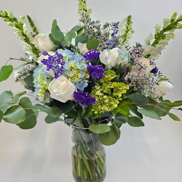 Bouquet of white roses, blue hydrangeas, and purple flowers in a glass vase