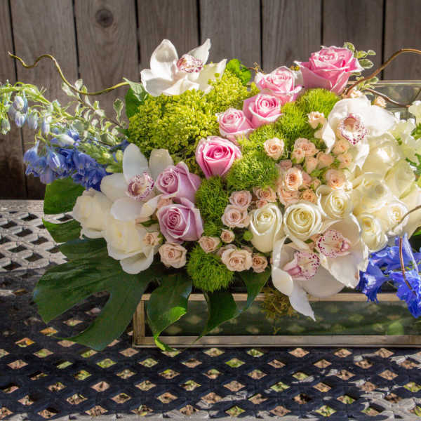 Mixed floral arrangement in a rectangular glass vase with pink, white, and blue blooms
