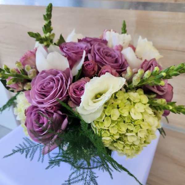 Low arrangement of lavender roses, white blooms, green hydrangea and trailing fern in a compact bouquet.