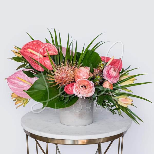 Pink tropical flower arrangement with ranunculus in a white ceramic vase on a marble table