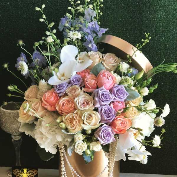 Large pastel rose and orchid arrangement in a gold hatbox with draped pearl garlands.
